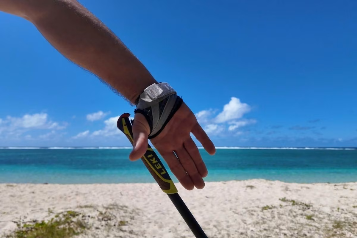 Main dans le gantelet d'un bâton de marche nordique, plage turquoise en arrière-plan