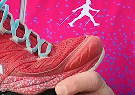 Chaussure de trail rose tenue en main, pare-pierres à l’avant et tige basse