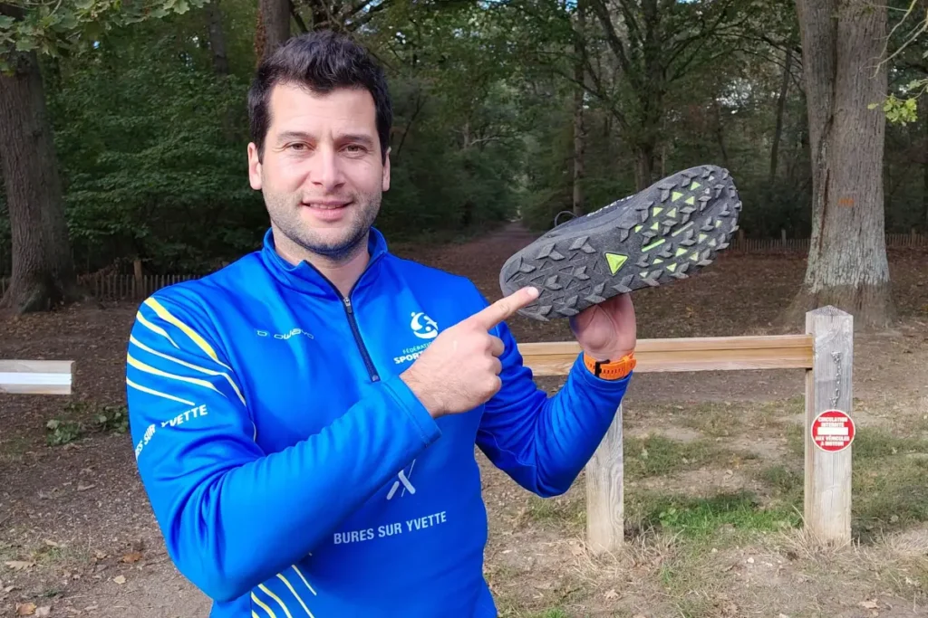 Kévin Richard montre la semelle crantée d’une chaussure de marche nordique, en forêt