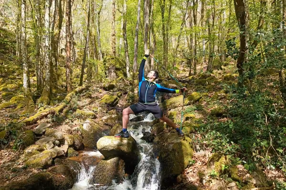 Kévin Richard sur un rocher au milieu d'une cascade en forêt, bâton levé