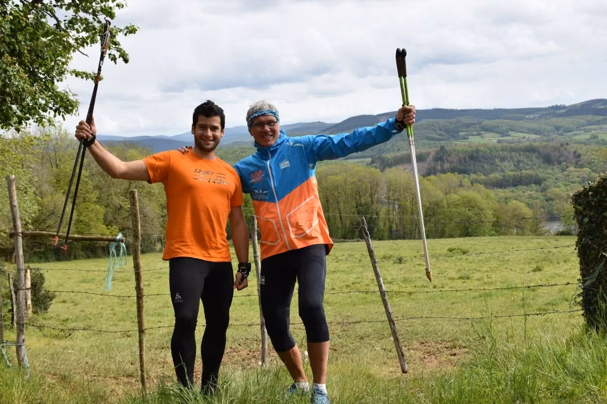 Deux marcheurs souriants, bâtons levés, face à la vallée