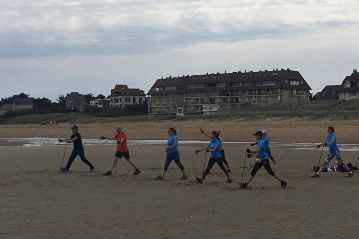 Groupe en marche nordique sur une plage devant des villas