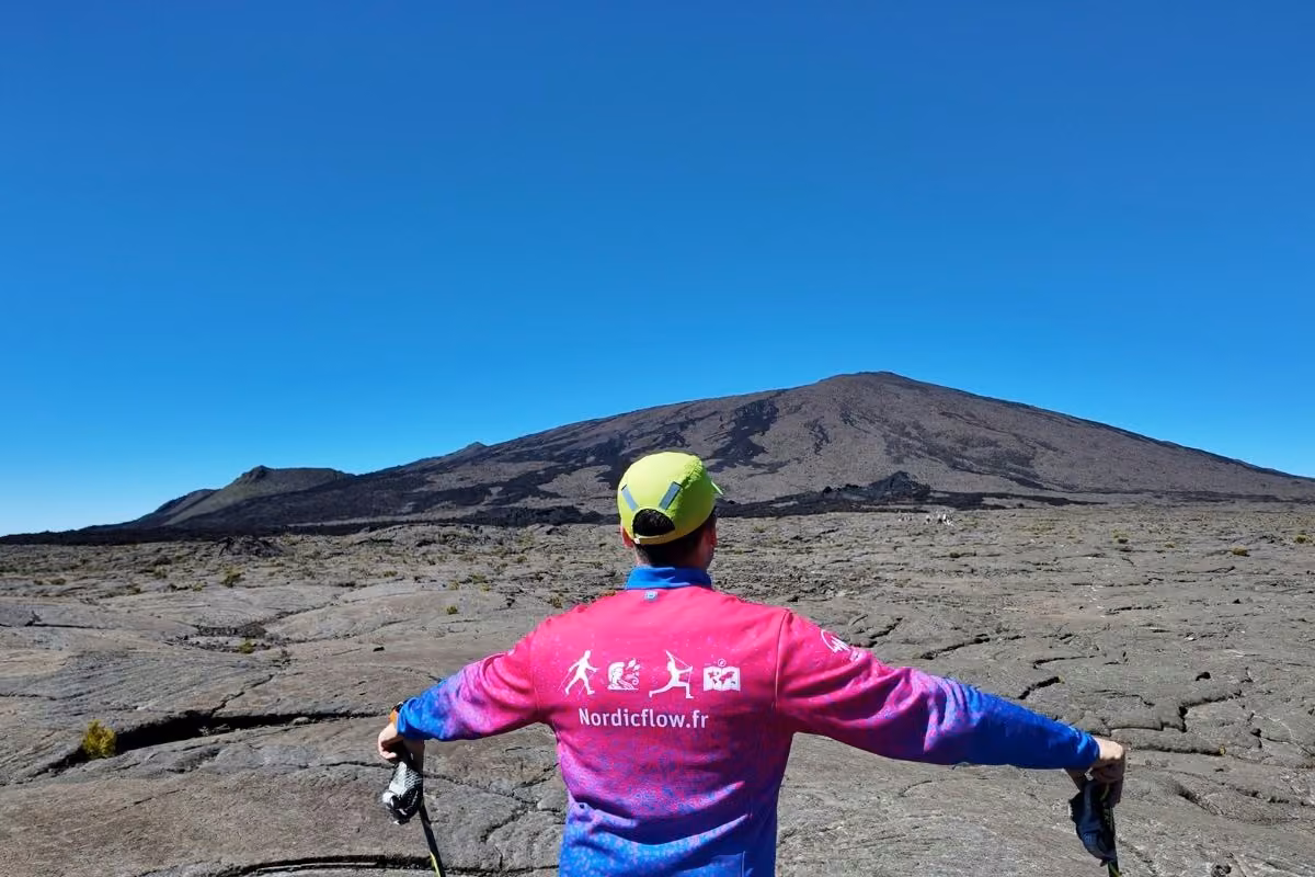 Marcheur de dos en veste Nordic Flow, bras écartés devant un volcan de La Réunion