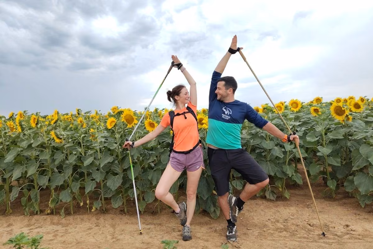 Kévin Richard et Lolita en équilibre sur une jambe, bâtons levés, devant un champ de tournesols