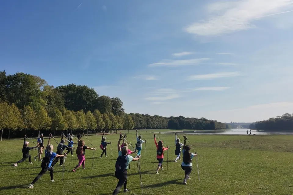 Groupe en posture de Nordic Yoga® avec bâtons sur la pelouse face au Grand Canal du parc du château de Versailles