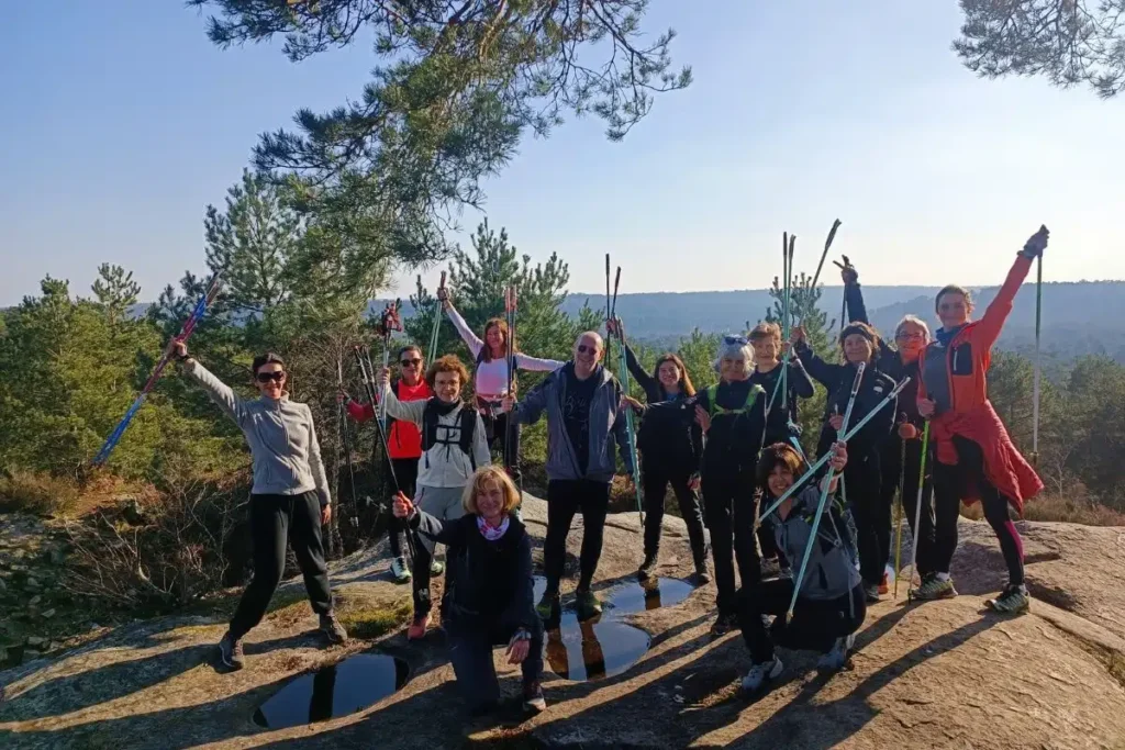Groupe Nordic Flow souriant, bâtons levés, lors d'une sortie de marche nordique en forêt