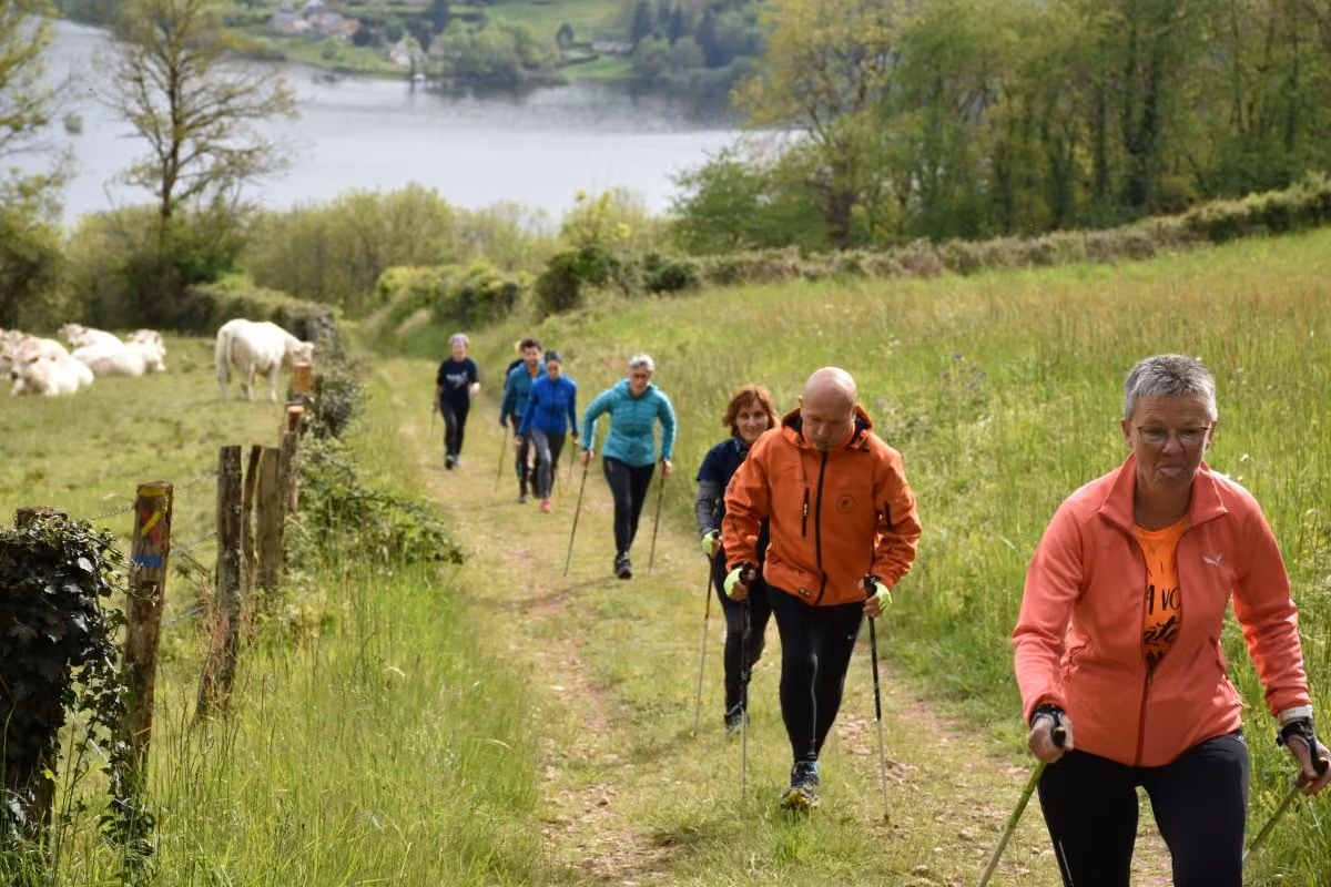 Groupe de marche nordique montant un chemin d’herbe au-dessus d’un lac du Morvan